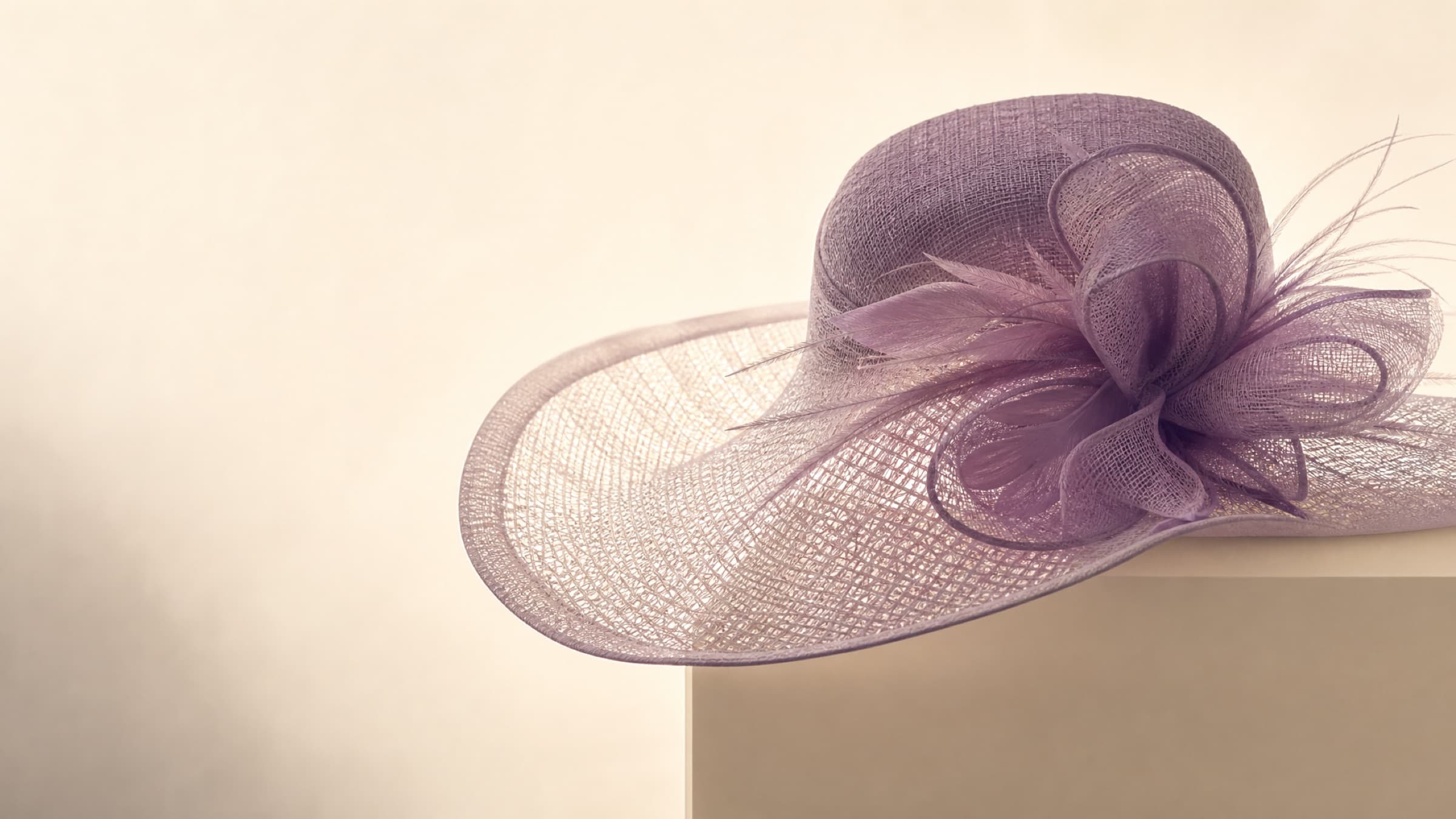 A wide-brim occasion hat photographed against the light, the weave of the brim visible through it