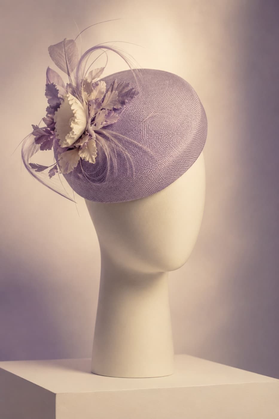 Structured cocktail hat seen in profile on a featureless display block