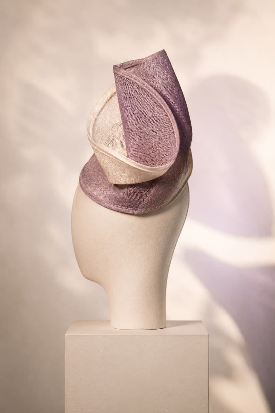 A sculpted fascinator in afternoon light on a featureless display block
